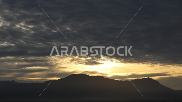 السماء الملبدة بالغيوم السوداء اثناء غروب الشمس، الشمس المغطاة بالغيوم السوداء، القمم والمرتفعات الجبلية، الطبيعة الجبلية وقت غروب الشمس، خلفية الطبيعة الجبلية
