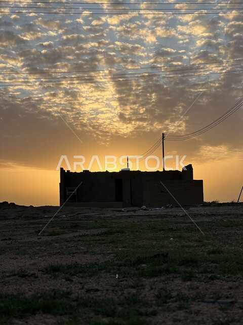 السماء الملبدة بالغيوم وقت غروب الشمس، اعمدة واسلاك الكهرباء، منزل قديم وسط ارض صحراوية خالية، مناظر طبيعية اثناء غروب الشمس