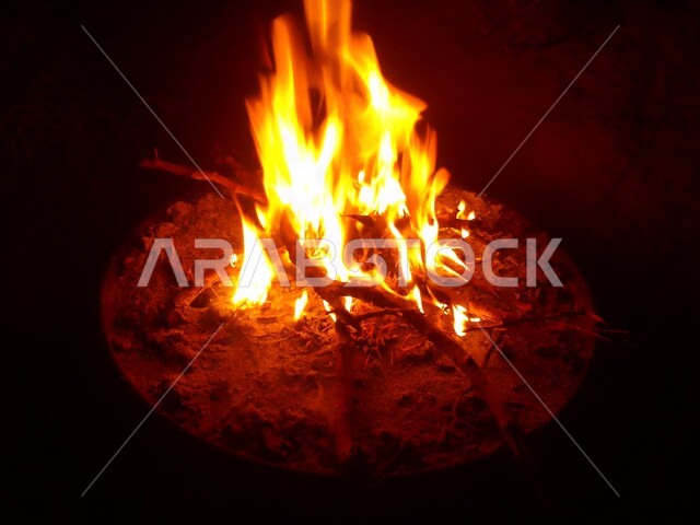 النيران المشتعلة في الحطب ليلاً ، اللهب الأحمر المشتعل في رحلة تخييم في الصحراء ، الطبيعة في صحراء المملكة العربية السعودية ليلاً ، البر و التخييم