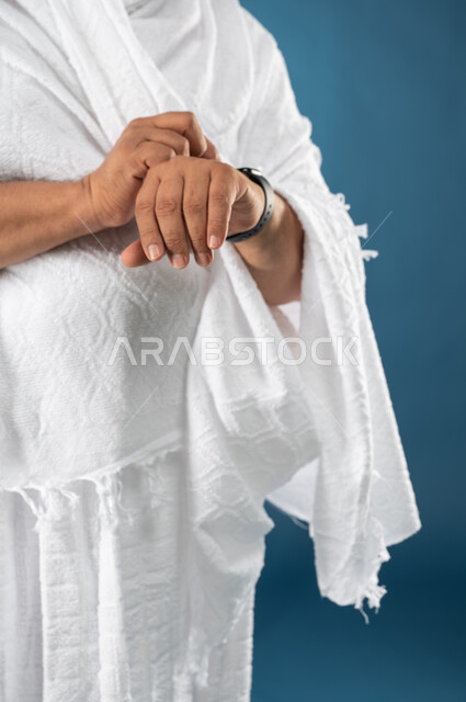معرفة وتحديد الوقت، مفهوم ادارة الوقت، بورتريه مقرب لرجل مسن مسلم عربي سعودي خليجي يرتدي ملابس الاحرام ويستخدم ساعة يد الكترونية، موسم الحج 2023، آداء مناسك الحج والعمرة، الركن الخامس من أركان الاسلام، خلفية زرقاء