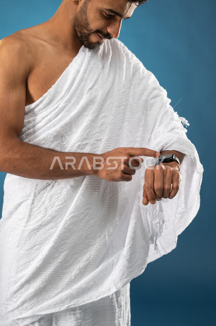 Knowing and determining time, the concept of time management, a close-up portrait of a Saudi Arabian Gulf Muslim young man wearing ihram clothes and using an electronic wristwatch, Hajj season 2023, performing Hajj and Umrah rituals, the fifth pillar of I