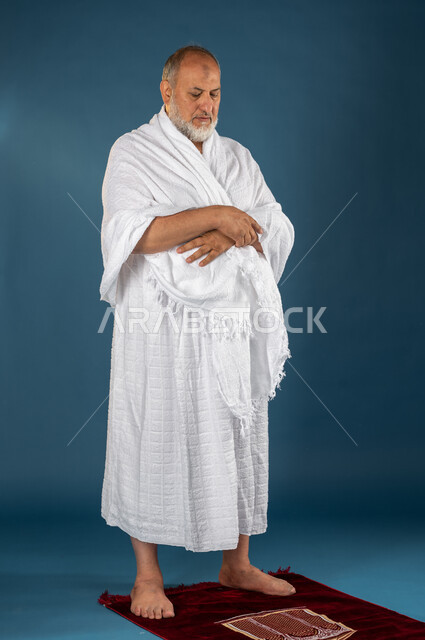 Performing the obligatory prayer, a portrait of an elderly Saudi Muslim Gulf man wearing ihram clothes and sitting on the prayer rug, performing the rituals of Hajj and Umrah, praying and drawing closer to God, the fifth pillar of Islam, Hajj season 2023,