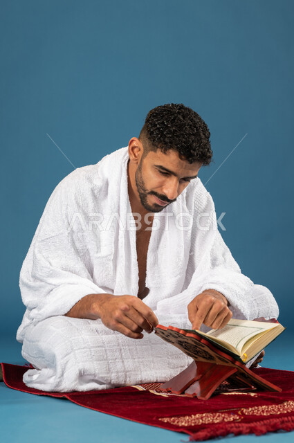 حفظ وتفسير القران الكريم، بورتريه لشاب مسلم خليجي سعودي يجلس على سجادة الصلاة ويقوم بقراءة وتلاوة القران، ارتداء ملابس الاحرام، آداء مناسك الحج والعمرة، الركن الخامس من أركان الاسلام، موسم الحج 2023، خلفية زرقاء