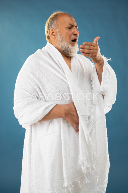 ارتداء ملابس الاحرام، العطاس والانفلونزا، بورتريه لرجل مسن مسلم عربي سعودي خليجي مريض يعطس، إيماءات وجه تدل على المرض والتعب، آداء مناسك الحج والعمرة، الركن الخامس من أركان الاسلام، موسم الحج 2023، خلفية زرقاء