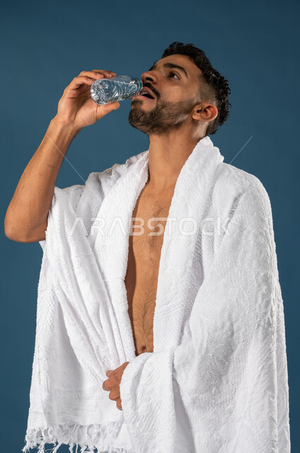 الاستمتاع بشرب مياه زمزم، بورتريه لشاب مسلم عربي سعودي خليجي يرتدي ملابس الاحرام، الارتواء بالمياه العذبة، اداء مناسك الحج والعمرة، الركن الخامس من أركان الاسلام، موسم الحج 2023، خلفية زرقاء