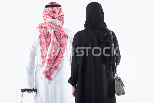 بورتريه من الخلف لزوج عربي خليجي سعودي يمسك بيده حقيبة سفر يقف بجانب زوجته استعداداً لرحلة سياحية ، جولة سياحية ، سياحة و سفر ، قضاء أوقات ممتعة ، خلفية بيضاء