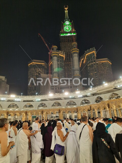 Pilgrims of the Sacred House of God in the courtyards of the Holy Mosque of Mecca, the clock tower in Makkah Al-Mukarramah in the Kingdom of Saudi Arabia at night, performing the rituals of Hajj and Umrah, sacred Islamic religious places and monuments