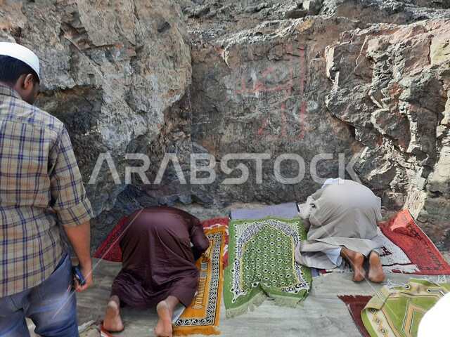 رجال عرب خليجيين سعوديين مسلمين يقومون باداء فريضة الصلاة على جبال المدينة المنورة في المملكة العربية السعودية، السجود على سجادة الصلاة، القمم والمرتفعات الجبلية، جبال المدينة المنورة الصخرية، تضاريس الطبيعة الجبلية في السعودية