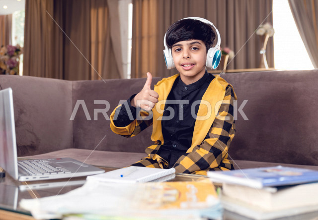تلميذ سعودي خليجي يرتدي سماعة الراس ،  يدرس في المنزل بتعابير وجه مختلفة ، يتابع حصص الاونلاين عن طريق الحاسوب المحمول  ، التعلم عن بعد ، مفهوم التعليم عبر الانترنت ، التعليم المنزلي اثناء الحجر الصحي و تفشي فيروس كورونا ، العزلة الذاتية .