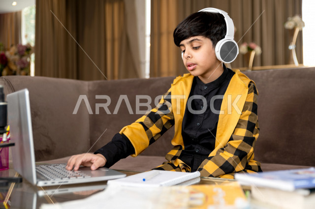 تلميذ سعودي خليجي يرتدي سماعة الراس ،  يدرس في المنزل بتعابير وجه مختلفة ، يتابع حصص الاونلاين عن طريق الحاسوب المحمول  ، التعلم عن بعد ، مفهوم التعليم عبر الانترنت ، التعليم المنزلي اثناء الحجر الصحي و تفشي فيروس كورونا ، العزلة الذاتية .