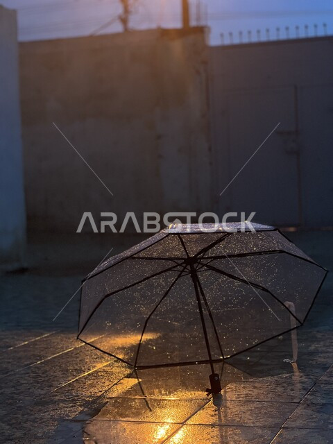 An umbrella that protects from rain in a transparent color on the ground with raindrops in the city of Jazan, rainy winter weather, the concept of protection from rain.