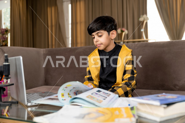 A Saudi Gulf student studying at home with different facial expressions, following online classes via a laptop, distance learning, the concept of online education, home education during quarantine and the outbreak of the Corona virus, self-isolation