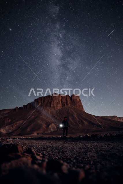  رجل يمسك بيده مصباح كهربائي يقف في ارض صحراويه امام حافة العالم، المناطق الطبيعية الجبلية, مطل الجراند كانيون, المعالم التاريخية الاثرية الصحراوية , أماكن سياحيه مشهورة, منظر السماء المرصعة بالنجوم .