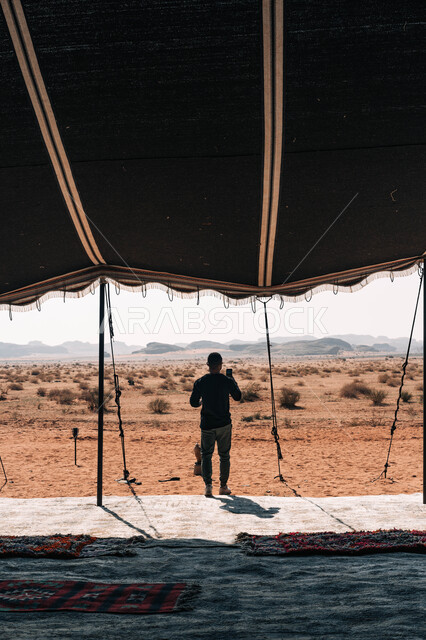 صورة من الخلف ل رجل يقف في ارض صحراويه امام حافة العالم ويلتقط الصور التذكارية عبر الهاتف المحمول، مطل الجراند كانيون, المناطق الطبيعية الجبلية, المعالم التاريخية الاثرية الصحراوية , أماكن سياحيه مشهورة,