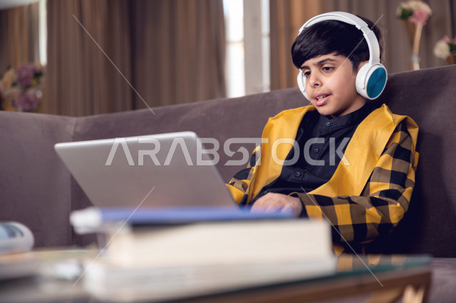 تلميذ سعودي خليجي يرتدي سماعة الراس ،  يدرس في المنزل بتعابير وجه مختلفة ، يتابع حصص الاونلاين عن طريق الحاسوب المحمول  ، التعلم عن بعد ، مفهوم التعليم عبر الانترنت ، التعليم المنزلي اثناء الحجر الصحي و تفشي فيروس كورونا ، العزلة الذاتية .
