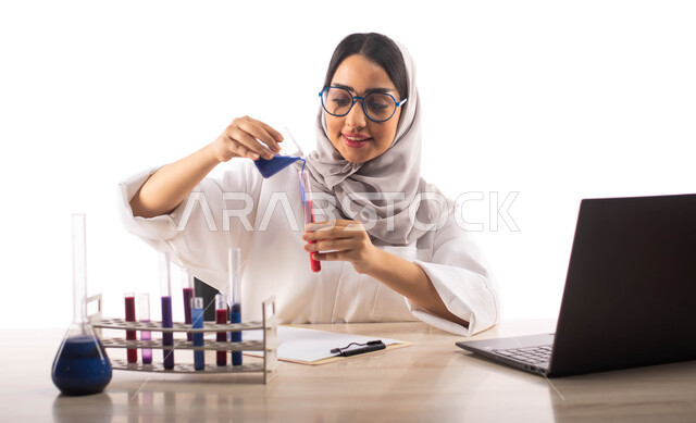 Conducting experiments in the laboratory using test tubes, gestures indicating joy and happiness, sitting in the chemistry laboratory, a portrait of a veiled Saudi Arabian Gulf medical laboratories and analysis doctor wearing a white medical coat and hold