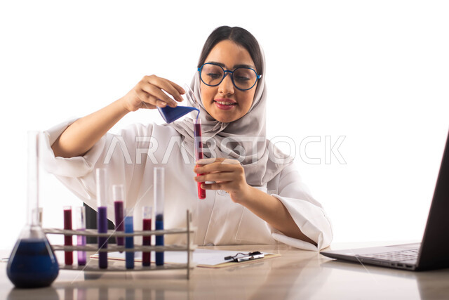 اجراء التجارب في المختبر باستخدام انابيب الاختبار ,ايماءات تدل على الفرح والسعادة, الجلوس في معمل الكيمياء ، بورتريه لطبيبة مختبرات وتحاليل طبية عربية خليجية سعودية محجبة ترتدي المعطف الطبي الابيض و تحمل بيدها انبوب زجاجي ، التفاعلات الكيميائية ،البحث وال