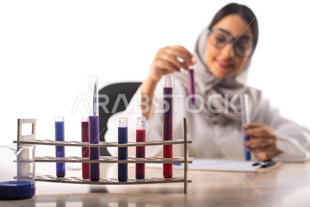 ايماءات تدل على الفرح والسعادة, الجلوس في معمل الكيمياء ، بورتريه لطبيبة مختبرات وتحاليل طبية عربية خليجية سعودية محجبة ترتدي المعطف الطبي الابيض و تحمل بيدها انبوب زجاجي , استخدام انابيب الاختبار لاجراء التجارب في المختبر ، التفاعلات الكيميائية ،البحث وا