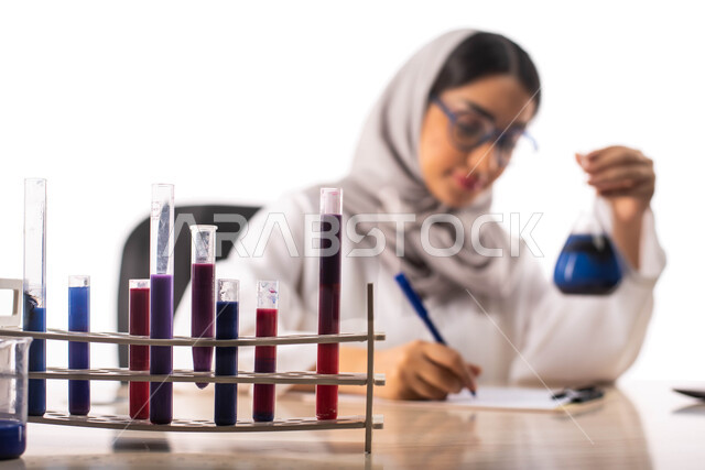 تدوين الملاحظات والنتائج ،الجلوس في معمل الكيمياء ، بورتريه لطبيبة عربية خليجية سعودية محجبة ترتدي المعطف الطبي الابيض وتحمل بيدها انبوب زجاجي, استخدام انابيب الاختبار لاجراء التجارب في المختبر ، التفاعلات الكيميائية ،البحث والتطوير ، مفهوم الكيمياء الحيو