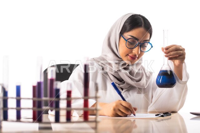 تدوين الملاحظات والنتائج ،الجلوس في معمل الكيمياء ، بورتريه لطبيبة عربية خليجية سعودية محجبة ترتدي المعطف الطبي الابيض وتحمل بيدها انبوب زجاجي, استخدام انابيب الاختبار لاجراء التجارب في المختبر ، التفاعلات الكيميائية ،البحث والتطوير ، مفهوم الكيمياء الحيو