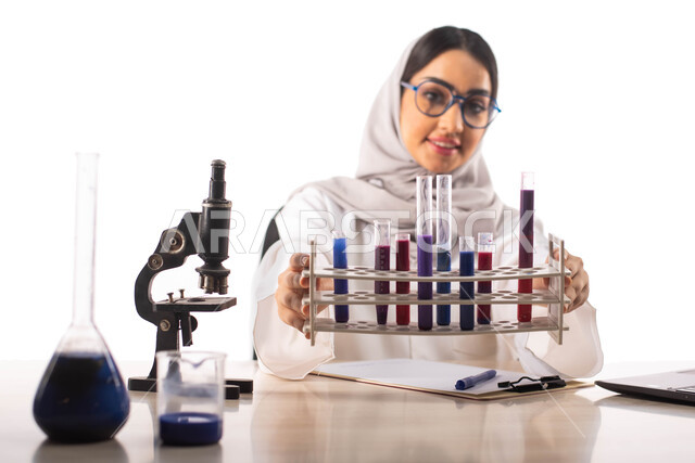البحث والتطوير ، الجلوس في معمل الكيمياء ، بورتريه لطبيبة مختبرات وتحاليل طبية عربية خليجية سعودية محجبة ترتدي المعطف الطبي الابيض والنظارات الطبية وتحمل بيدها انابيب الاختبار لاجراء التجارب في المختبر ، التفاعلات الكيميائية ، مفهوم الكيمياء الحيوية, خلفي