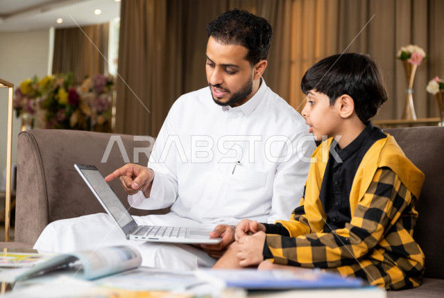 تلميذ سعودي خليجي يدرس في المنزل مع والده ،الذي يتبع معه حصص الاونلاين عن طريق الحاسوب المحمول  ، التعلم عن بعد ، مفهوم التعليم عبر الانترنت ، التعليم المنزلي اثناء الحجر الصحي و تفشي فيروس كورونا ، العزلة الذاتية .