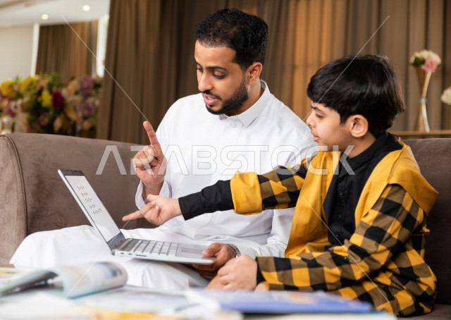 تلميذ سعودي خليجي يدرس في المنزل مع والده ،الذي يتبع معه حصص الاونلاين عن طريق الحاسوب المحمول  ، التعلم عن بعد ، مفهوم التعليم عبر الانترنت ، التعليم المنزلي اثناء الحجر الصحي و تفشي فيروس كورونا ، العزلة الذاتية .