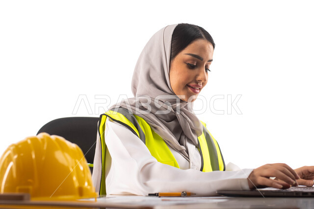ايماءات تدل على السعادة , وظائف ومهن ، استخدام أدوات ومعدات هندسية على مخطط تصميم هندسي ، ارتداء بدلة السلامة, بورتريه لمهندسة معمارية عربية خليجية سعودية محترفه داخل مكتب هندسي ، إستخدام جهاز الحاسوب المحمول للإنجاز وتتبع المهام ، خوذة الوقاية الصفراء ،خ