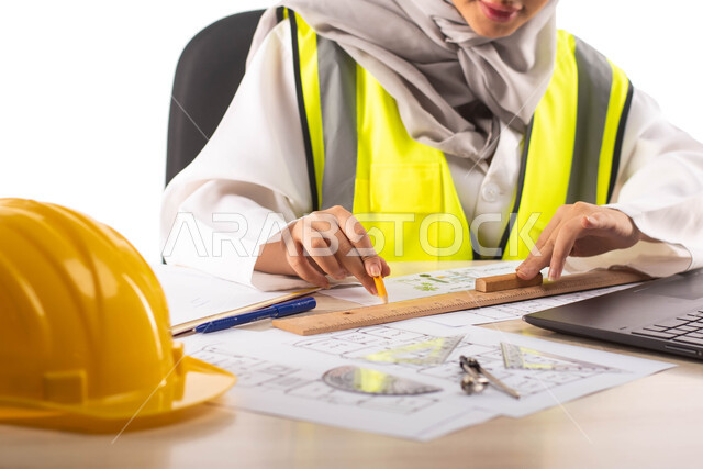  إستخدام جهاز الحاسوب المحمول للإنجاز وتتبع المهام ،  استخدام أدوات ومعدات هندسية على مخطط تصميم هندسي ، ارتداء بدلة السلامة, بورتريه لمهندسة معمارية عربية خليجية سعودية محترفه داخل مكتب هندسي ،خوذة الوقاية ،مهن ووظائف ، خلفية بيضاء
