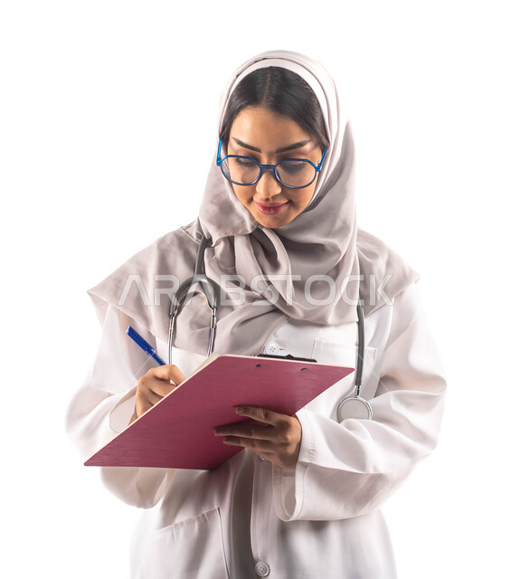 تسجيل البيانات على ملف تشخيص المريض, العمل في القطاع الصحي, بورتريه لطبيبة عربية سعودية خليجية محجبة ومبتسمة, تحمل بيدها ملف خاص بالمرضى، ارتداء المعطف الطبي والنظارات الطبية, مفهوم الطب والرعاية الصحية ، مهن و وظائف  ، خلفية بيضاء