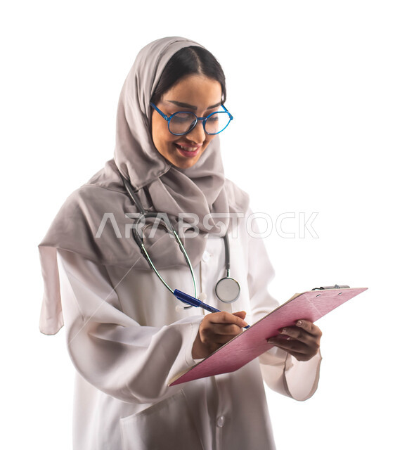 ايماءات تدل على السعادة, تسجيل البيانات على ملف تشخيص المريض, العمل في القطاع الصحي, بورتريه لطبيبة عربية سعودية خليجية محجبة ومبتسمة, تحمل بيدها ملف خاص بالمرضى، ارتداء المعطف الطبي والنظارات الطبية, مفهوم الطب والرعاية الصحية ، مهن و وظائف  ، خلفية بيضا