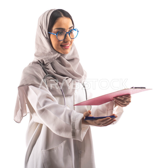 استقبال المرضى في العيادة, العمل في القطاع الصحي, ايماءات تدل على السعادة, بورتريه لطبيبة عربية سعودية خليجية محجبة ومبتسمة, تحمل بيدها ملف خاص بالمرضى، ارتداء المعطف الطبي والنظارات الطبية, مفهوم الطب والرعاية الصحية ، مهن و وظائف  ، خلفية بيضاء