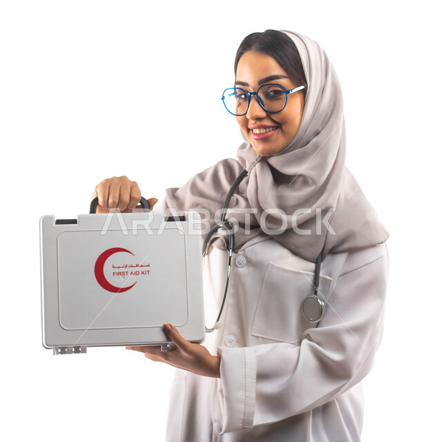 المعدات الطبية اللازمة, بورتريه لطبيبة عربية سعودية خليجية محجبة ومبتسمة, تحمل بيدها حقيبة الإسعافات الأولية ، ارتداء المعطف الطبي والنظارات الطبية, مفهوم الطب والرعاية الصحية ، مهن و وظائف ، مفهوم الخدمات و الطوارئ الطبية ، خلفية بيضاء 