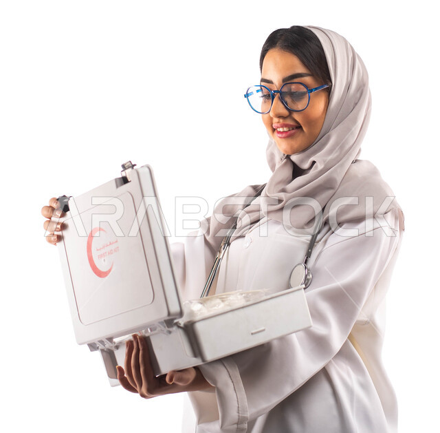The concept of medical services and emergencies, the necessary medical equipment, a portrait of a smiling, veiled Saudi Arabian Gulf doctor, carrying a first aid kit in her hand, wearing a medical coat and medical glasses, the concept of medicine and heal