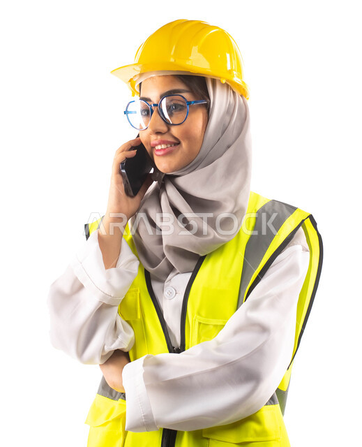 وظائف ومهن ،اجراء مكالمة هاتفية  عبر الجوال, ايماءات تدل على السعادة والفرح, بورتريه لمهندسة انشاءات معمارية عربية سعودية خليجية مبتسمة ترتدي النظارات الطبية ، ارتداءالخوذة وبدلة السلامة الخاصة في العمل ،مخططات وتصاميم هندسية، خلفية بيضاء