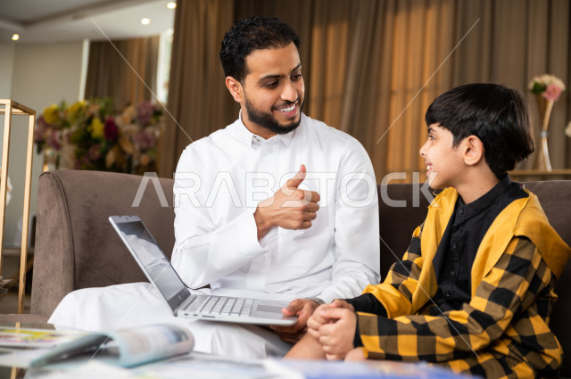 تلميذ سعودي خليجي يدرس في المنزل مع والده ،الذي يتبع معه حصص الاونلاين عن طريق الحاسوب المحمول  ، التعلم عن بعد ، مفهوم التعليم عبر الانترنت ، التعليم المنزلي اثناء الحجر الصحي و تفشي فيروس كورونا ، العزلة الذاتية .