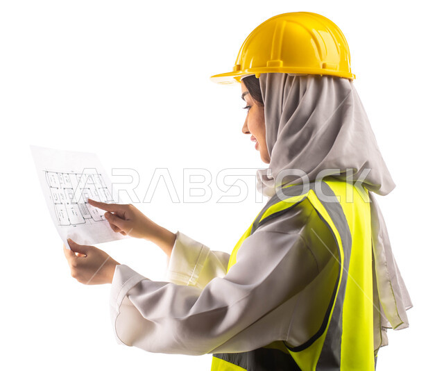 ارتداءالخوذة وبدلة السلامة الخاصة في العمل ، بورتريه من الجانب لمهندسة انشاءات معمارية عربية سعودية خليجية محترفة تحمل بيدها مخطط البناء وتشير الى شيئ ما ، مخططات وتصاميم هندسية، مهن ووظائف هندسية، خلفية بيضاء