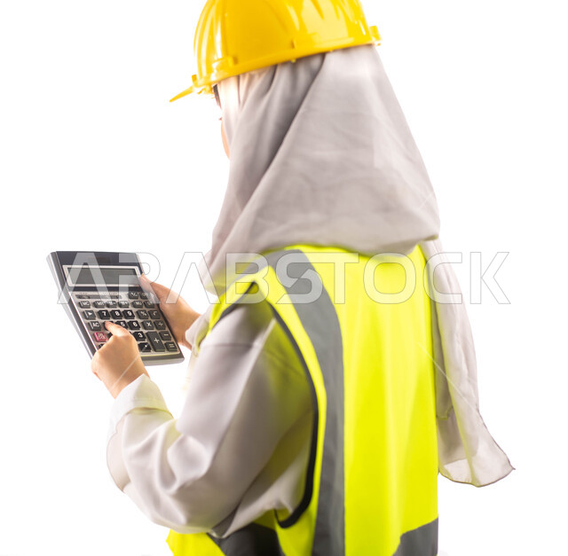 استخدام الآلة الحاسبة لإجراء العمليات الحسابية ,مخططات و تصماميم هندسية, ادارة المشاريع الهندسية، بورتريه من الخلف لمهندسة معمارية عربية خليجية سعودية محترفة ترتدي خوذة وسترة الحماية الخاصة بالعمل, مهن و وظائف هندسية .