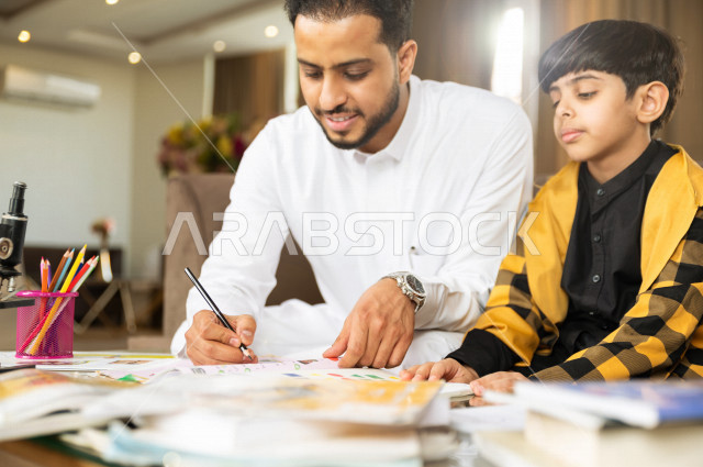 A Saudi Gulf student studying at home with his father, helping him to do his homework, distance learning, the concept of online education, home education during quarantine and the outbreak of the Corona virus, self-isolation.