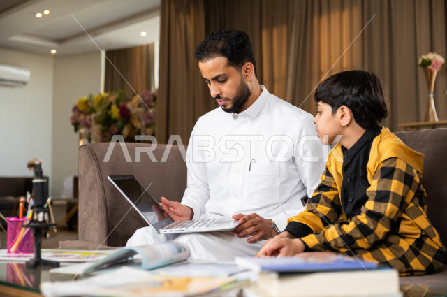تلميذ سعودي خليجي يدرس في المنزل مع والده ،الذي يتبع معه حصص الاونلاين عن طريق الحاسوب المحمول  ، التعلم عن بعد ، مفهوم التعليم عبر الانترنت ، التعليم المنزلي اثناء الحجر الصحي و تفشي فيروس كورونا ، العزلة الذاتية .