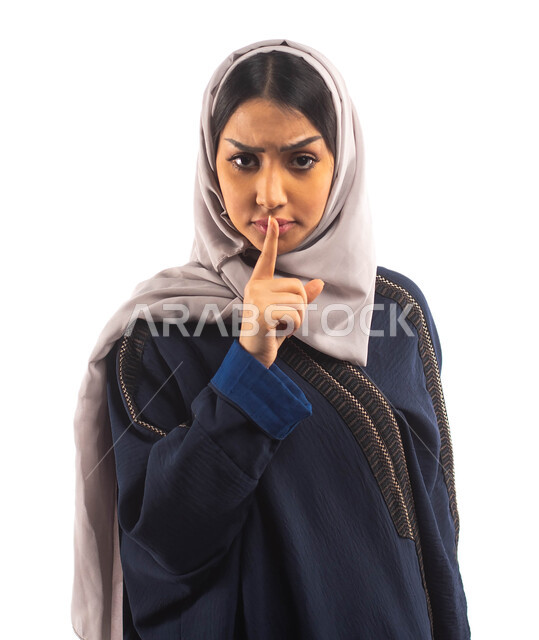 تعابير وجه تدل على الغضب , بورتريه لأمرأه عربية خليجية سعودية محجبة ترتدي العباءه السوداء ,إيماءات يدين تدل على طلب الهدوء و عدم الإزعاج, التوقف عن الكلام, الأمر بالصمت والسكوت , خلفية بيضاء