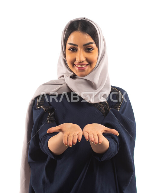 تحمل بين يديها عنصر هولوجرامي ،بورتريه لأمرأه عربية خليجية سعودية محجبة ترتدي العباءة السوداء تنظر إلى الكاميرا ، تعرض شيء ما ، ايماءات تدل على السعادة, خلفية بيضاء