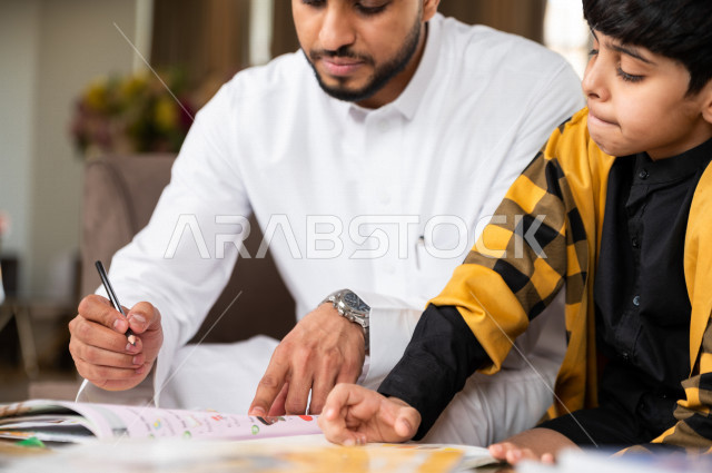 تلميذ سعودي خليجي يدرس في المنزل مع والده ، يساعده على تأدية واجباته المدرسية ، التعلم عن بعد ، مفهوم التعليم عبر الانترنت ، التعليم المنزلي اثناء الحجر الصحي و تفشي فيروس كورونا ، العزلة الذاتية .