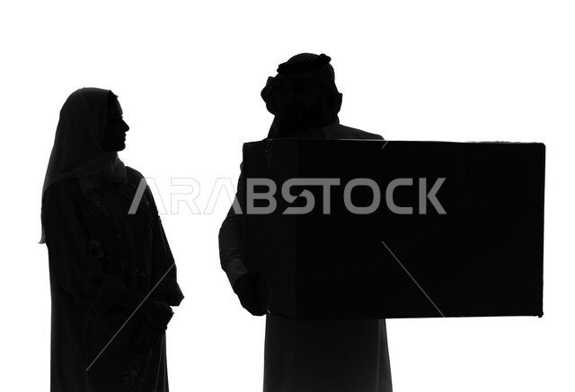 الانتقال ونقل العفش لبيت جديد, ترتيب وتنظيم المنزل، صناديق وحاويات كرتونية، بورتريه صورة ظلية لزوجان خليجيان عربيان سعوديان يقومان بنقل صناديق الأغراض المنزلية، امتلاك سكن جديد والاستقرار العائلي، اسكان وتمليك، خلفية بيضاء, سيلوليت