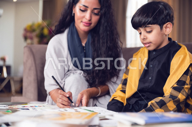 تلميذ سعودي خليجي يدرس في المنزل مع والدته ، تساعده على تأدية واجباته المدرسية ، التعلم عن بعد ، مفهوم التعليم عبر الانترنت ، التعليم المنزلي اثناء الحجر الصحي و تفشي فيروس كورونا ، العزلة الذاتية .