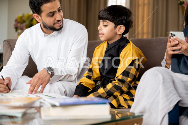 تلميذ سعودي خليجي يدرس في المنزل مع والده ، يساعده على تأدية واجباته المدرسية ، التعلم عن بعد ، مفهوم التعليم عبر الانترنت ، التعليم المنزلي اثناء الحجر الصحي و تفشي فيروس كورونا ، العزلة الذاتية .