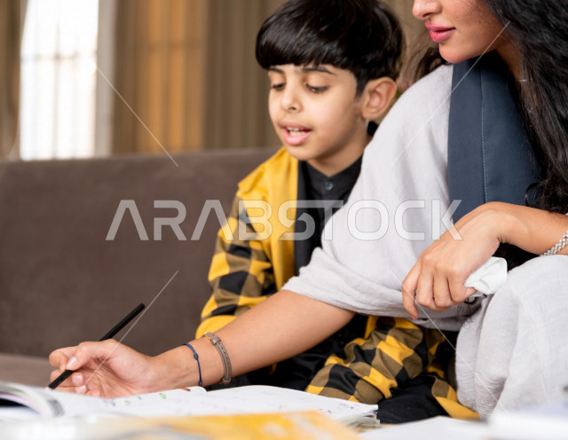 A Saudi Gulf student studying at home with his mother, helping him to do his homework, distance learning, the concept of online education, home education during quarantine and the outbreak of the Corona virus, self-isolation.
