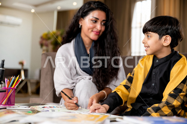 A Saudi Gulf student studying at home with his mother, helping him to do his homework, distance learning, the concept of online education, home education during quarantine and the outbreak of the Corona virus, self-isolation.