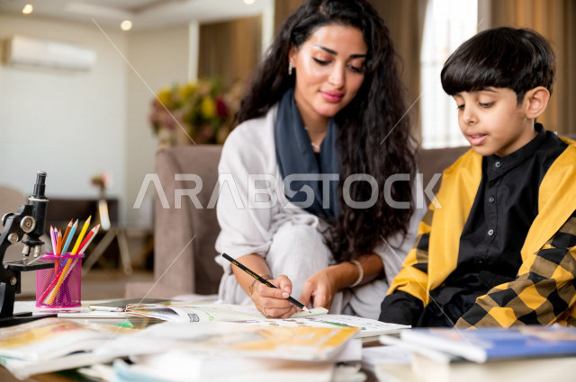 تلميذ سعودي خليجي يدرس في المنزل مع والدته ، تساعده على تأدية واجباته المدرسية ، التعلم عن بعد ، مفهوم التعليم عبر الانترنت ، التعليم المنزلي اثناء الحجر الصحي و تفشي فيروس كورونا ، العزلة الذاتية .