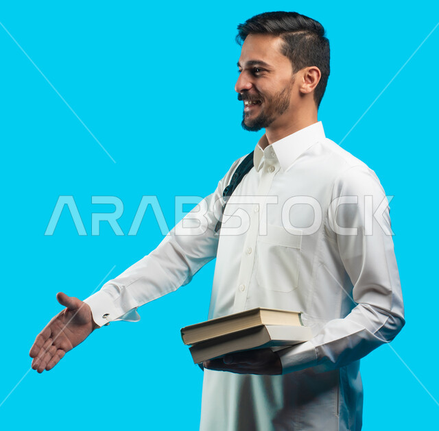إيماءات يدين تدل على المصافحة ، التعليم الجامعي في المملكة العربية السعودية ، تدوين الملاحظات وكتابة تقارير وأبحاث علمية ، بورتريه طالب جامعي عربي سعودي يرتدي الزي الخليجي و يحمل بيده كتب ، مراجعة الدروس اليومية ، خلفية زرقاء